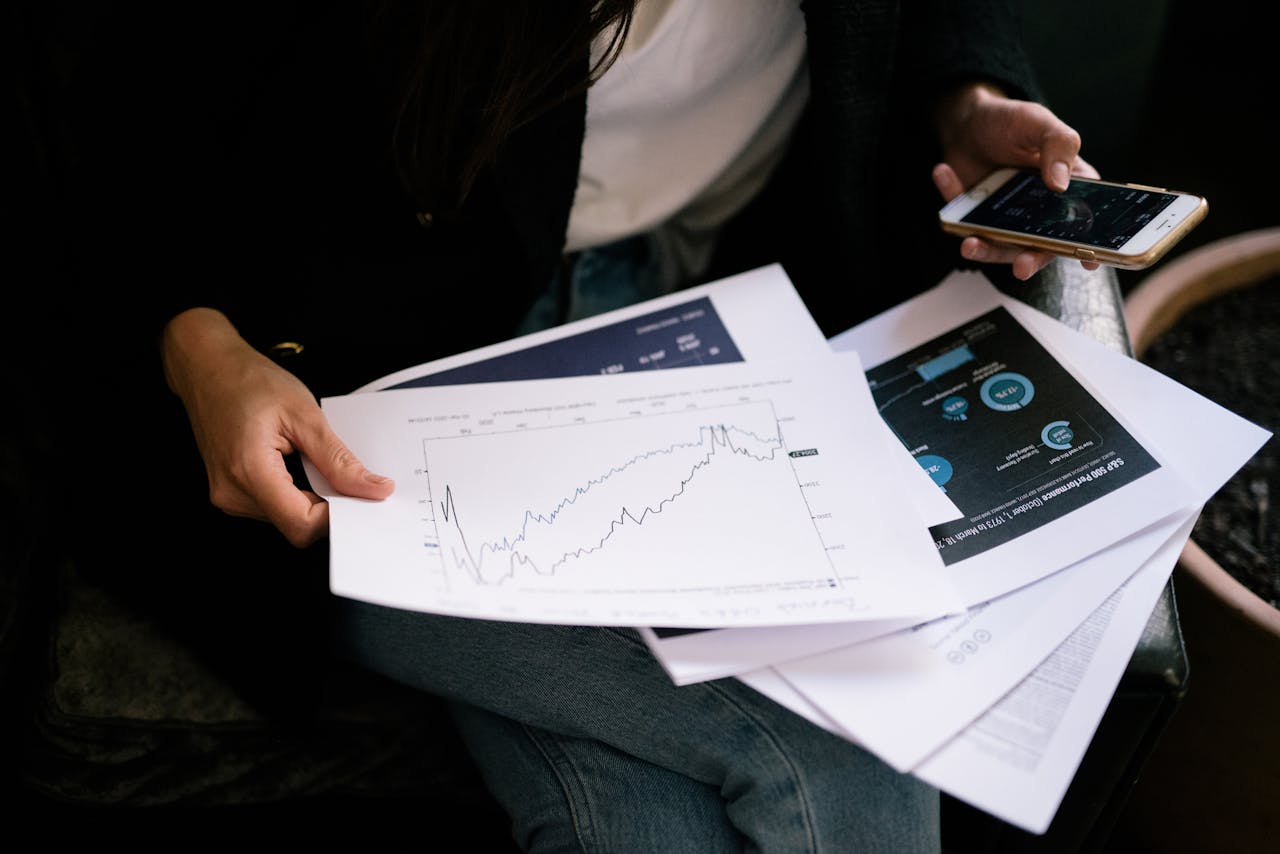 our-story A person reviews stock market graphs on paper and smartphone for business insights.